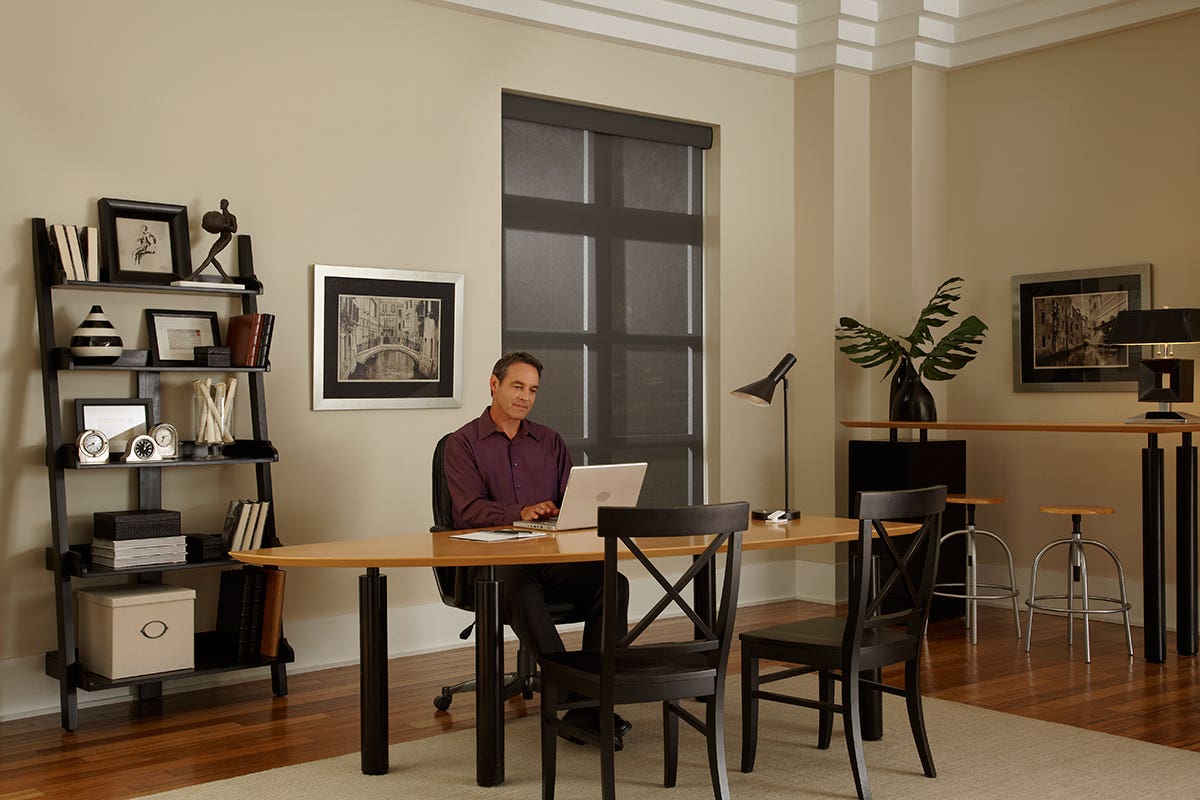 Man working in home office with fully closed sheer roller shades in charcoal gray