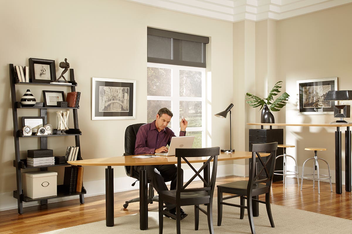 Man working in home office with open sheer roller shades in charcoal gray