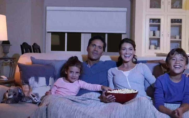 Family of four sitting on couch, watching tv and eating popcorn with white motorized shades in window behind them